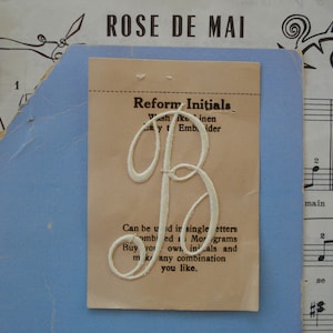 May include: A white card with the text "Reform Initials" and instructions on how to use the product. The card also features a white embroidered letter "B" in the center.