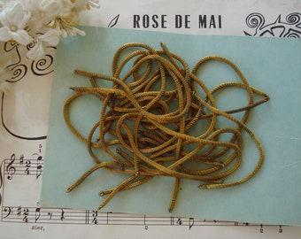 May include: A pile of gold-colored, coiled wire, resembling a spring, on a light blue background. The wire is approximately 10 inches long.