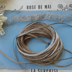 May include: A spool of silver and brown metallic ribbon with the text "ROSE DE MAI" and "LA SURPRISE" on a blue background.