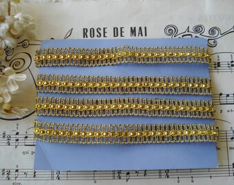 May include: Four rows of gold trim with a beaded design on a blue background. The trim is made of gold thread and beads. The background is a light blue card with the text "ROSE DE MAI" printed on it.