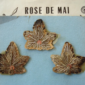 May include: Three leaf-shaped appliqués featuring metallic silver bullion wire embroidery and small gold-toned sequins. Each piece is crafted with a central vein and radiating wire details, arranged on a light blue card labeled ROSE DE MAI.