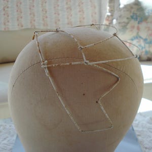 May include: A white wire hat form with a rusty wire frame. The wire frame is shaped like a crown.