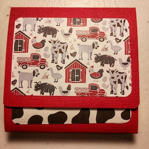 May include: A red, folded paper card with a farm animal theme. The top section features a patterned design with cows, pigs, chickens, and a red truck. The bottom section has a black and white cowhide pattern.