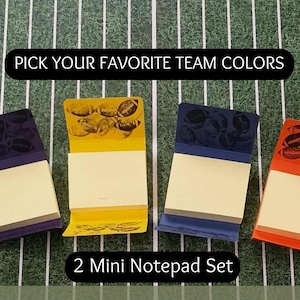 May include: A set of four mini notepads in football edition. Each notepad features a different team color: purple, yellow, blue, and orange. The notepads have football graphics and the text "Team Spirit" and "Pick Your Favorite Team Colors".
