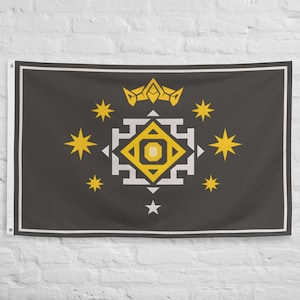 May include: A dark gray flag with a white border and a central geometric design. The design features a yellow crown, yellow stars, and a white and yellow square pattern. The flag is hanging on a white brick wall.