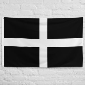May include: A black and white flag with a white cross on a black background. The flag is hanging on a white brick wall.
