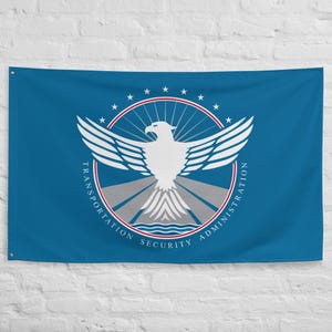May include: A blue flag featuring the Transportation Security Administration (TSA) logo. The logo includes a white eagle with outstretched wings, surrounded by a red and white circle with stars. The words "TRANSPORTATION SECURITY ADMINISTRATION" are printed around the circle.