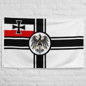 Puede incluir: Una bandera blanca con un diseño de cruz negra y un emblema circular con un águila negra coronada. La bandera también incluye una sección negra y roja con una cruz negra.