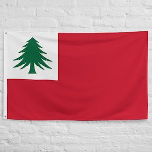 May include: A rectangular red flag with a white section in the top left corner, displaying a green pine tree. The flag is hanging against a white brick wall. A historical symbol.