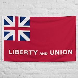 Könnte beinhalten: Eine rote Flagge mit einem blau-weißen Emblem in der oberen linken Ecke und den weißen Worten "LIBERTY AND UNION". Die rechteckige Flagge hängt vor einer weißen Backsteinmauer.