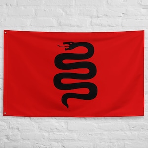 May include: A red flag with a black snake design. The snake is stylized and centered on the flag. The flag is hanging against a white brick wall.