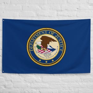 Peut inclure: Un drapeau bleu avec le sceau du Département de la Justice. Le sceau circulaire présente un aigle brun, du texte et des étoiles. Le drapeau rectangulaire est suspendu contre un mur blanc.