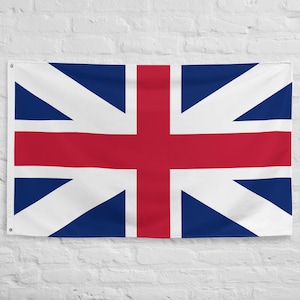 May include: A rectangular flag featuring the Union Jack design, with a white background and a combination of red and blue geometric shapes. The flag is hanging against a white brick wall.