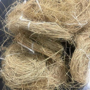 Pode incluir: Vários feixes de grama seca castanho-clara, amarrados com barbante branco. A grama parece estar pronta para uso. Os feixes são bem compactados, dando uma aparência natural e orgânica.