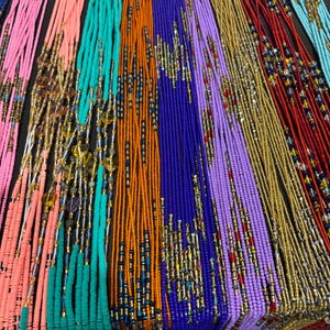 Könnte beinhalten: Eine Sammlung farbenfroher Perlenketten in verschiedenen Farbtönen, darunter Rosa, Orange, Türkis, Lila und Gold. Die Halsketten sind eng angeordnet und zeigen die Vielfalt der Designs und Farben. Einige Halsketten haben dekorative Akzente.