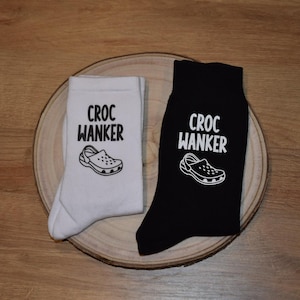 May include: Two pairs of crew socks, one white and one black, each bearing the text "CROC WANKER" and a Croc shoe graphic. The socks are presented on a wooden platter.