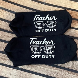 May include: Two pairs of black no-show socks. Each sock features the white text "Teacher OFF DUTY" with a graphic of sunglasses reflecting palm trees and the ocean.