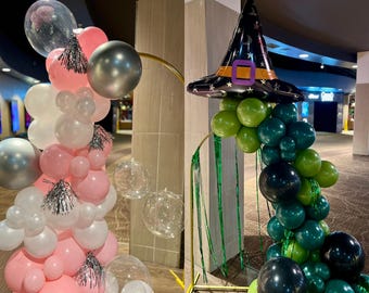 May include: Two balloon arches, one pink and silver, the other green and black. The pink arch features pink, white, and silver balloons, with clear bubble balloons. The green arch has a witch hat balloon at the top, with green and black balloons.
