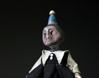 May include: A handmade doll with a painted face, wearing a black dress with a white collar and a blue and white party hat.