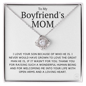 May include: A silver necklace with a knot pendant and a clear crystal in the center. The necklace comes in a white box with the text "To My Boyfriend's MOM" and a message expressing gratitude for raising a wonderful son.