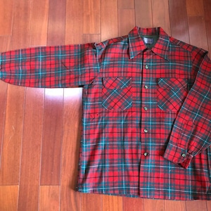 May include: A red, green, and white plaid flannel shirt with a button-down collar and two chest pockets.