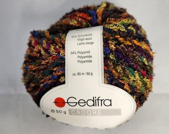 May include: A ball of yarn with a mix of brown, gold, red, green, and blue colours. The yarn is made of 46% virgin wool and 54% polyamide. The label reads "Gedifra CADORE" and "ca. 80 m / 50 g".