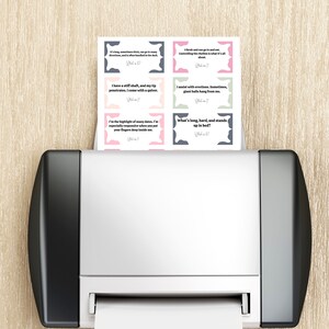 May include: A printer is shown with a stack of printed cards. Each card has a unique question and answer. The cards are in various colors, including pink, gray, and white. The text on the cards is in black.