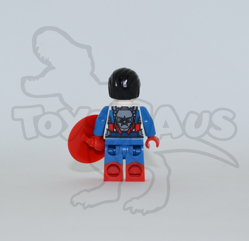 May include: A red, white and blue Lego minifigure of Captain America. The figure is wearing a blue and red suit with a white star on the chest. The figure is holding a red shield in its right hand. The figure is standing on a white background.