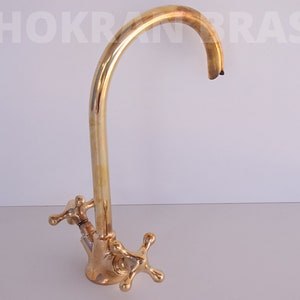 May include: A gold-toned kitchen faucet with a high arc spout and two cross-shaped handles.