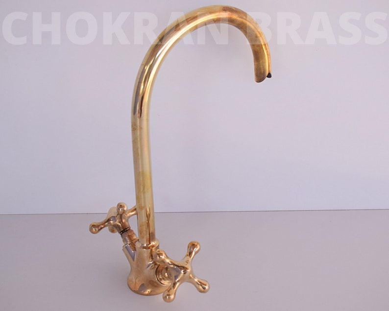 May include: A gold-toned kitchen faucet with a high arc spout and two cross-shaped handles.