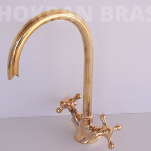 May include: A gold-toned brass kitchen faucet with a high-arc spout and two cross-shaped handles.