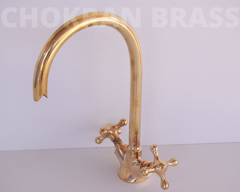 May include: A gold-toned brass kitchen faucet with a high-arc spout and two cross-shaped handles.