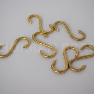Może przedstawiać: Zestaw ośmiu złotych haczyków w kształcie litery S. Haczyki są wykonane z metalu i mają gładkie wykończenie.