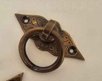 May include: A brass door handle with a decorative ring and a diamond-shaped plate with intricate floral designs.