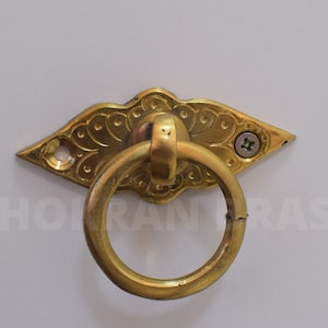 Peut inclure: Une poignée de tirage en métal doré avec un design orné. La poignée est fixée à une plaque décorative avec un motif floral.