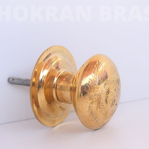 Peut inclure: Une poignée de porte dorée avec un motif complexe. La poignée est ronde et a une plaque arrière plate.