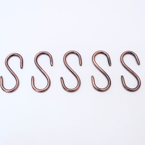 May include: Five copper-colored S-shaped hooks. The hooks are all the same size and shape.