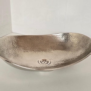 May include: A hammered nickel oval bathroom sink. The sink has a textured surface and a drain in the centre. The sink is a light silver colour and has a smooth rim.