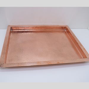 May include: A rectangular copper tray with a hammered finish. The tray has a raised rim and is perfect for serving or displaying items.