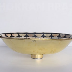 Op de afbeelding: Een ovale gouden kom met een decoratieve zwart-witte moza&iuml;ekrand rond de rand. De kom heeft een ronde basis en is gemaakt van metaal.