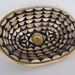 Op de afbeelding: Ovale decoratieve kom met een geometrisch patroon in zwart en wit gemaakt van bot en messing. De kom heeft een messing rand en een klein gaatje in het midden.