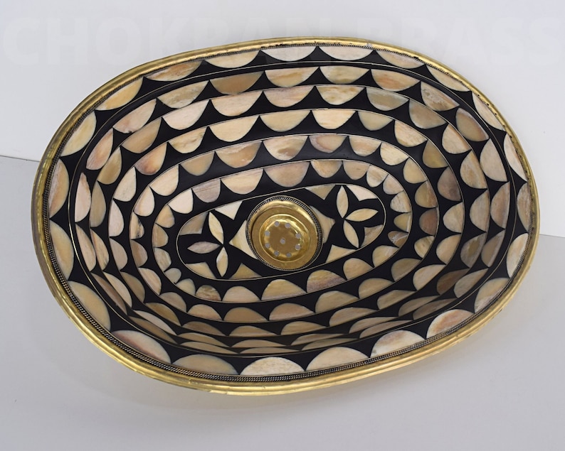 Op de afbeelding: Ovale decoratieve kom met een geometrisch patroon in zwart en wit gemaakt van bot en messing. De kom heeft een messing rand en een klein gaatje in het midden.