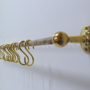 May include: Brass towel bar with a round knob on one end and a round wall mount on the other. The bar has 10 S-shaped hooks.