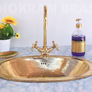 May include: A gold hammered oval bathroom sink with a matching soap dispenser and faucet. The sink is on a white marble countertop.