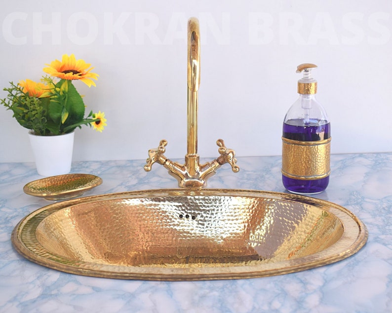 May include: A gold hammered oval bathroom sink with a matching soap dispenser and faucet. The sink is on a white marble countertop.