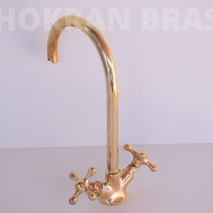 May include: A gold-toned kitchen faucet with a high arc spout and two cross-shaped handles.