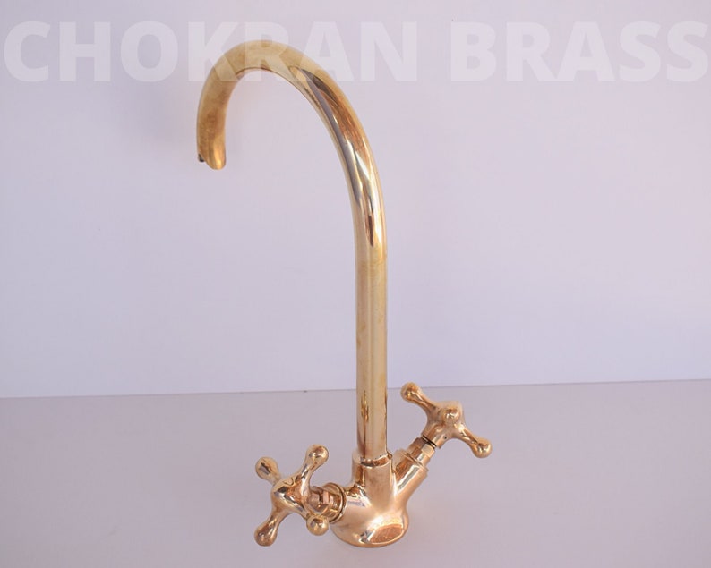 May include: A gold-toned kitchen faucet with a high arc spout and two cross-shaped handles.