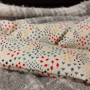 May include: A white fabric hand warmer with a colorful pattern of red, yellow, blue, and black leaves and dots.