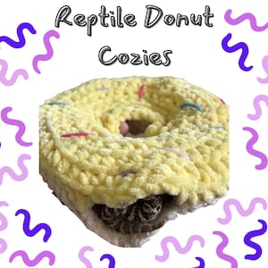 Può includere: Un'accogliente cuccia per rettili a forma di ciambella gialla all'uncinetto con zuccherini colorati. La cuccia ha un buco al centro e un rettile è all'interno. Il testo "Reptile Donut Cozies" è in alto.