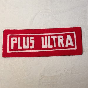 Peut inclure: Tapis rectangulaire rouge avec du texte blanc qui dit "PLUS ULTRA" dans une bordure blanche.